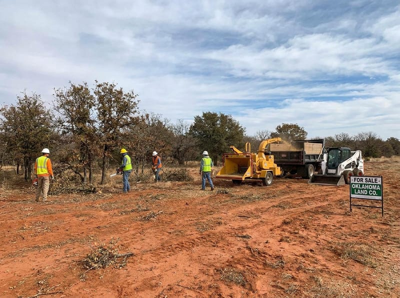 Crew clearing brush on an Oklahoma land lot with chipper and skid steer